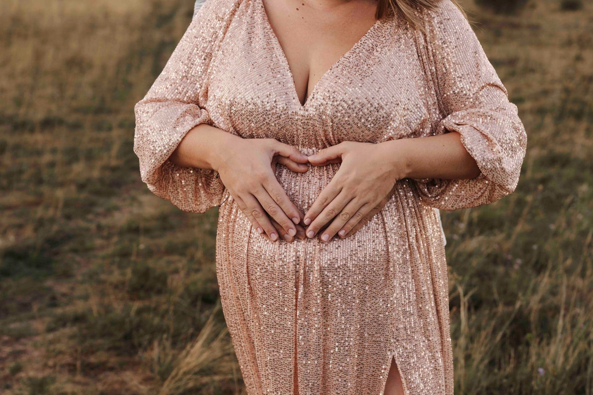 Babybauch Detailaufnahme – Herz aus Händen auf dem Bauch, Paillettenkleid im Abendlicht