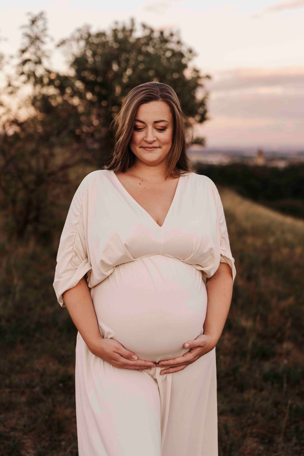 Babybauch Fotografie Wien – Lucia blickt auf ihren Bauch, Sonnenuntergang im Hintergrund