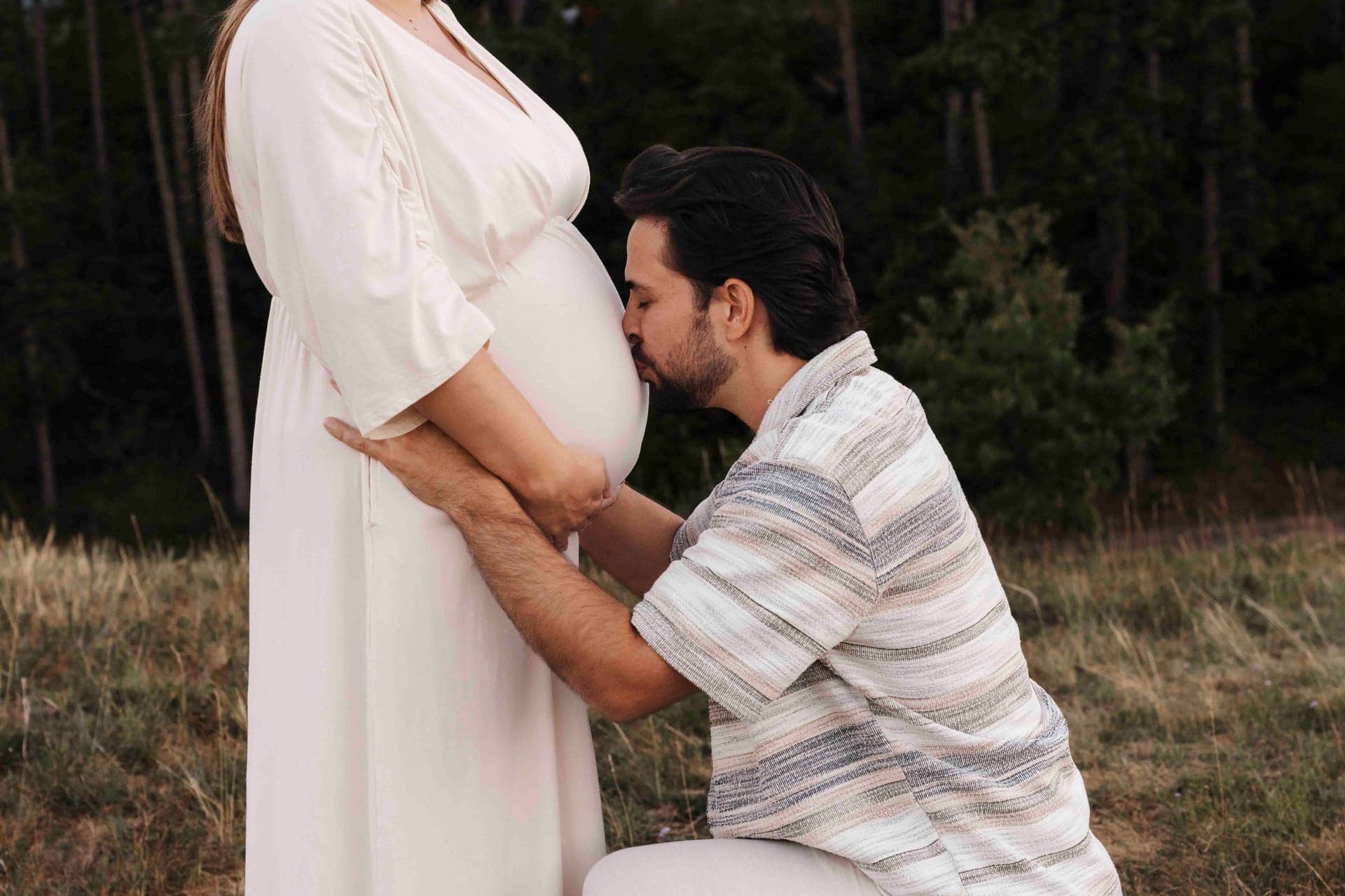 Babybauch Shooting mit Partner – werdender Papa kniet und küsst den Bauch, Outdoor Wien