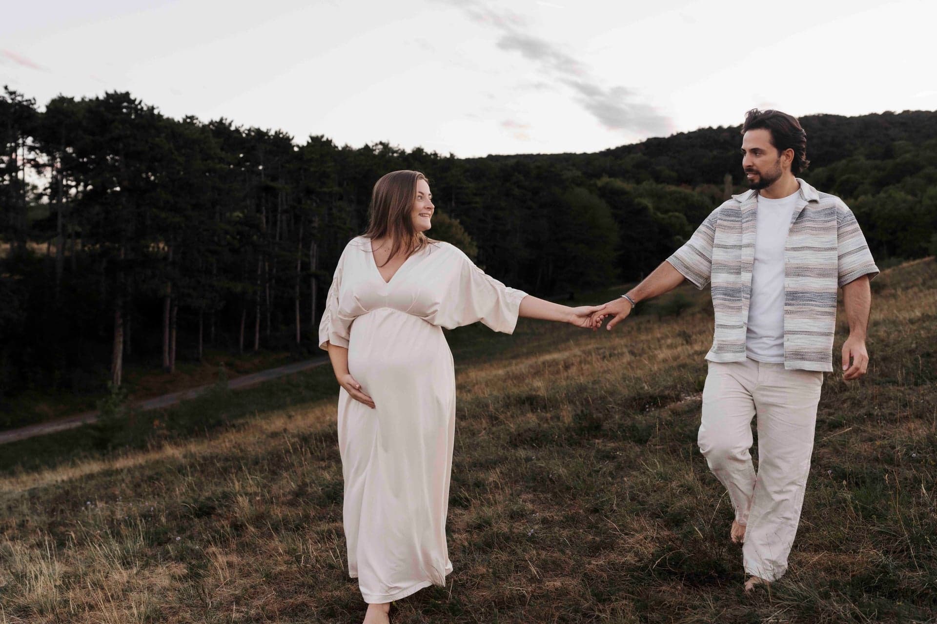 Babybauch Outdoor Shooting Wien – Paar geht Hand in Hand über die Wiese