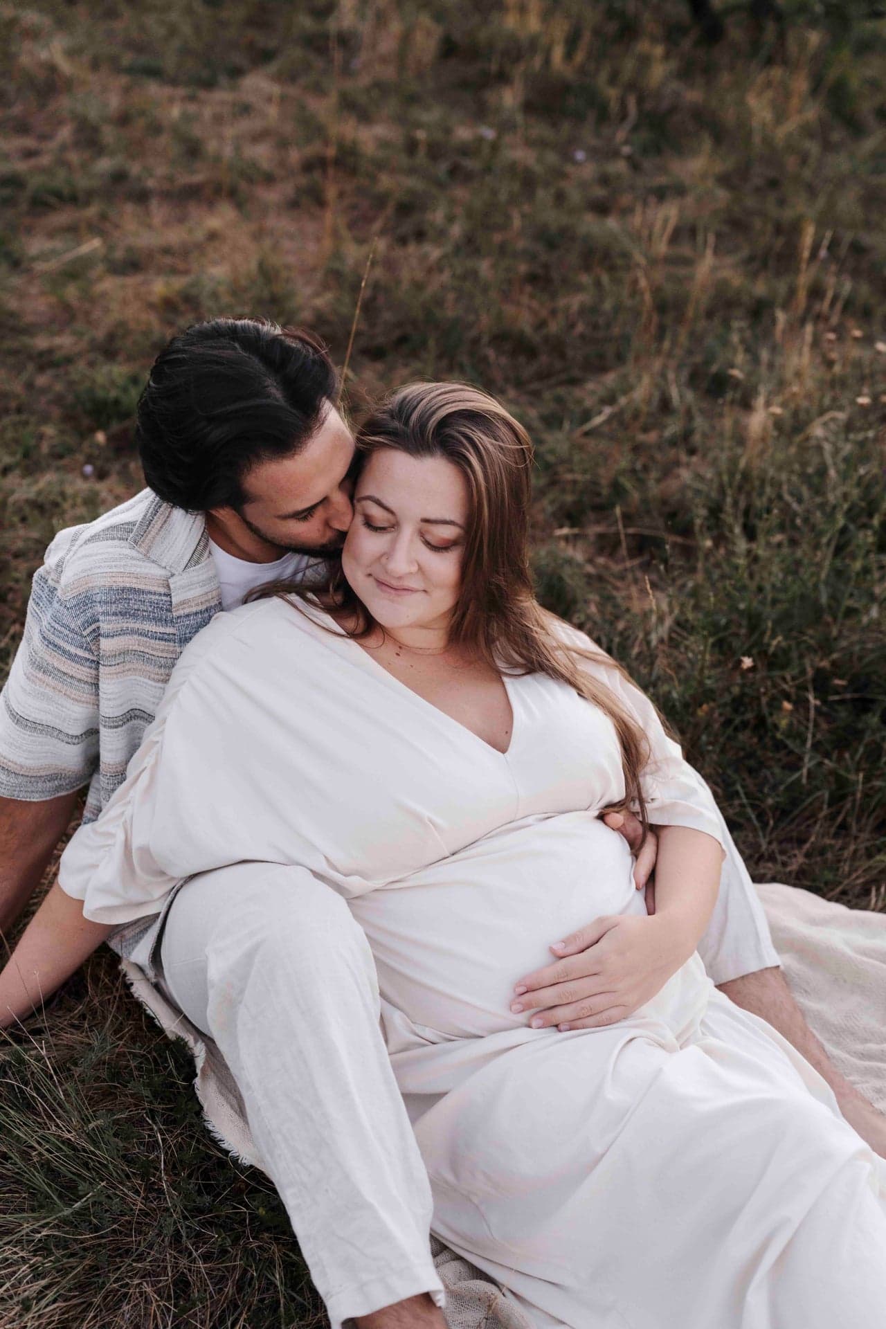 Babybauch Shooting Paar Wien – Max küsst Lucia auf die Schläfe, gemeinsam im Gras